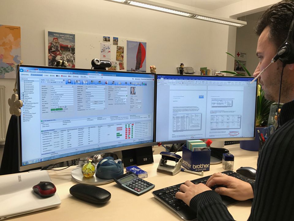 Imagebild Kontakt Dieses Imagebild für Kontaktangaben zeigt einen DRK-Mitarbeiter, der an einem Doppelmonitor mit dem rotkreuzCRM arbeitet.